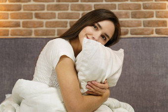 年轻的女人拥抱枕头舒适的床上白色床单