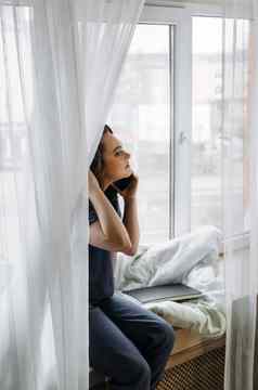 年轻的女人坐着窗台上会说话的电话