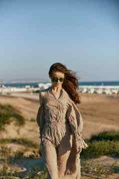 女人米色衣服站沙子度假胜地太阳镜享受温暖的天气