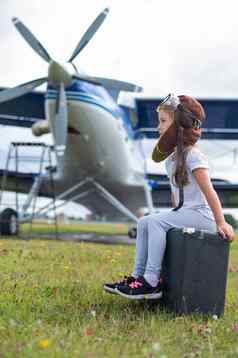 女孩飞行员的服装坐在手提箱背景飞机螺旋桨孩子梦想飞行天空
