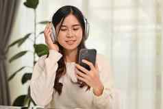 快乐年轻的女人穿无线耳机移动电话生活房间人技术生活方式概念