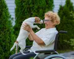上了年纪的高加索人女人拥抱杰克罗素梗狗坐着轮椅走在户外
