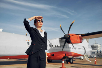 白天年轻的空姐正式的黑色的衣服站在户外飞机