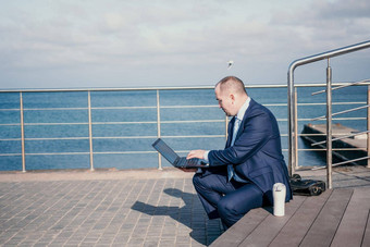 自信中间年龄商人工作远程在线打字移动PC键盘坐着海滩日落工作远程假期运行在线业务距离