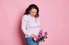 令人愉快的怀孕了女人郁金香微笑触碰肚子享受婴儿踢孤立的粉红色的背景