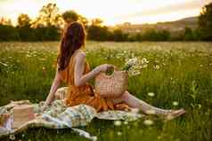 女人美丽的长整洁头发坐在橙色衣服洋甘菊场日落