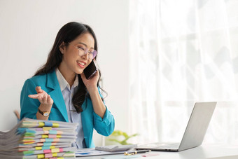 亚洲女人企业家忙工作办公室年轻的亚洲女人会说话的智能手机手机工作电脑桌子上