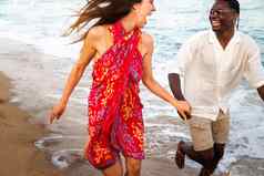 年轻的多民族的快乐夫妇运行海边假期旅行持有手
