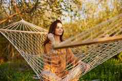快乐的女人坐着网吊床自然放松享受射线设置太阳温暖的夏天一天水平照片主题户外娱乐