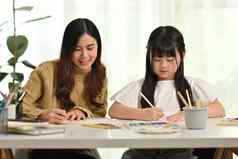 年轻的成人亚洲妈妈。可爱的女儿坐着表格家庭作业学习教育概念