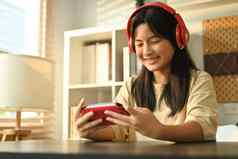 快乐的十几岁的亚洲女人穿耳机玩视频游戏可移植的游戏控制台