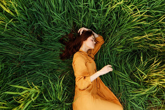 优雅的女人谎言高绿色草长夏天橙色衣服持有头发手享受自然阳光明媚的天气眼睛关闭