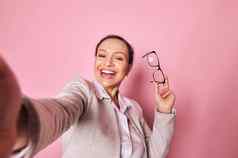 自拍快乐的女人持有眼镜微笑美丽的微笑相机孤立的粉红色的背景
