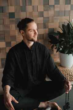 肖像年轻的男人。黑色的kimano坐着莲花位置健身房席室内