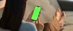 年轻的女人首页绿色屏幕模型智能手机坐着沙发生活房间