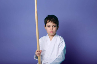 腰长度肖像迷人的宁静的自信孩子男孩合气道摔跤手持有木剑孤立的紫色的背景复制空间