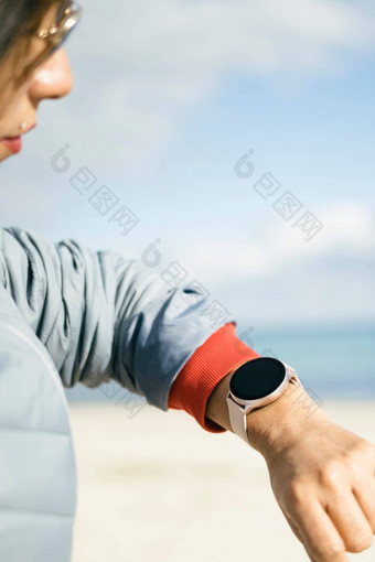 腰拍摄快乐浅黑肤色的女人女人穿着anorak检查健身结果智能手表提出了海滩海岸健康的生活方式
