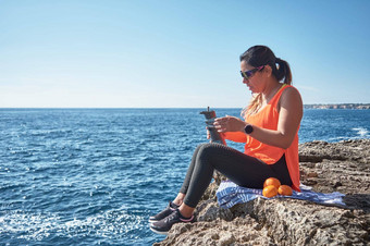 拉丁女人中年休息恢复强度吃喝水健身房会话燃烧卡路里保持适合在户外海穿耳机聪明的看