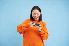 快乐微笑女孩年戏剧移动视频游戏持有智能手机手站蓝色的背景