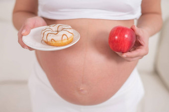 怀孕了女人持有红色的苹果甜甜圈选择食物