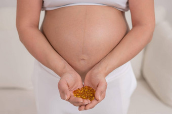 怀孕了女人只肚子持有一些维生素透明的金药片维生素准妈妈。