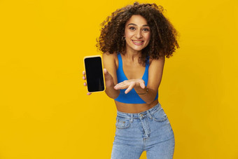 影响者女人电话手采取自拍会说话的视频调用自由职业者社会媒体技术工作卷曲的非洲式发型头发蓝色的衬衫黄色的背景微笑牙齿复制空间
