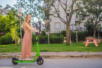 年轻的美丽的女人骑电踏板车工作现代女孩一代电运输生态生态运输日落电滑板