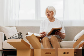 上了年纪的女人坐在沙发首页盒子收集的事<strong>情</strong>记<strong>忆</strong>专辑照片照片帧移动的地方清洁的事<strong>情</strong>快乐微笑生活方式退休