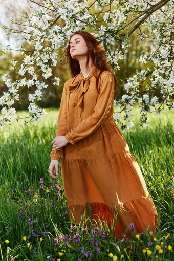 纤细的甜蜜的女人站长橙色衣服高草开花树衣服发展中光风