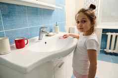 可爱的女孩持有牙刷相机站水槽浴室早....卫生例程