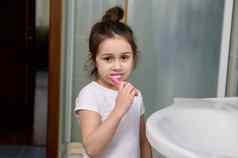 美丽的学龄前儿童女孩微笑相机刷牙牙齿站水槽首页浴室