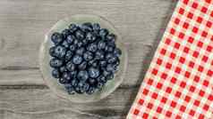 桌面视图小玻璃碗蓝莓红色的网纹条格平布桌布灰色的木桌子上
