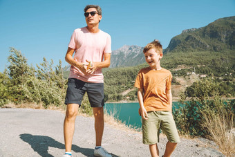 年轻的爸爸儿子站山视图孩子孩子男孩有趣的父亲徒步旅行徒步旅行山湖背景