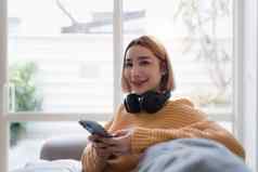 有吸引力的亚洲女人休息舒适的生活房间移动电话放松沙发生活方式