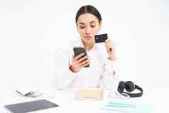 年轻的女人学生坐在智能手机信贷卡震惊了银行账户移动电话应用程序坐着沮丧白色背景