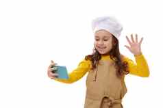 微笑积极的孩子女孩白色酋长他米色厨房围裙挥舞着手视频会议