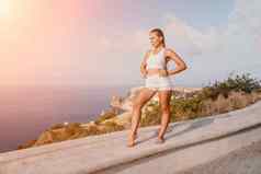 健身女人海快乐中间岁的女人白色运动服装练习早....在户外公园海滩视图女健身普拉提瑜伽例程概念健康的生活方式