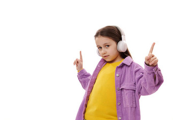 可爱的孩子女孩指出手指听很酷的配乐无线耳机孤立的白色