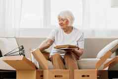 上了年纪的女人坐在沙发首页盒子收集的事情记忆专辑照片照片帧移动的地方清洁的事情快乐微笑生活方式退休