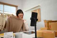 快乐的亚洲女在线卖方显示衣服前面相机记录视频博客视频生活流媒体首页办公室