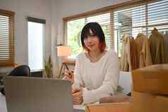 时尚的年轻的女小业务老板坐着工作桌子上纸板盒子移动PC
