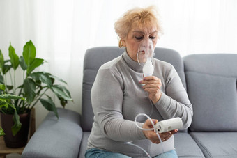 生病的高级女人病毒感染流感吃力的呼吸哮喘上了年纪的女吸入器喷雾器治疗坐着沙发首页