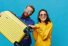 女人男人。微笑坐着手提箱黄色的手提箱微笑蓝色的背景包装旅行家庭假期旅行