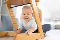 快乐婴儿攀爬传统的斯堪的那维亚设计师木高椅子现代明亮的首页可爱的婴儿微笑相机
