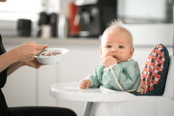 妈妈。勺子喂养婴儿男孩孩子婴儿椅子水果泥厨房首页婴儿固体食物介绍概念