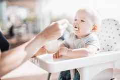 妈妈。勺子喂养婴儿男孩孩子婴儿椅子水果泥玄关夏天假期婴儿固体食物介绍概念