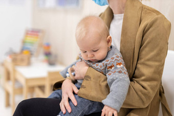 妈妈。持有婴儿婴儿男孩腿上坐着等待前面医生的办公室儿科检查孩子的健康护理概念