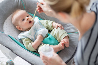 妈妈。勺子喂养婴儿男孩婴儿孩子婴儿椅子水果泥婴儿固体食物介绍概念