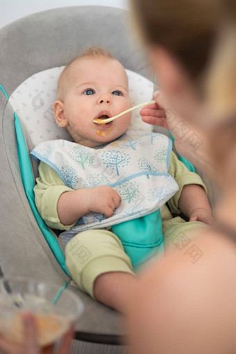 妈妈。勺子喂养婴儿男孩婴儿孩子婴儿椅子水果泥婴儿固体食物介绍概念
