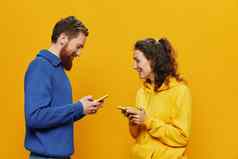 女人男人。快乐的夫妇手机手社会网络沟通弯曲的微笑有趣的战斗黄色的背景概念真正的家庭的关系自由职业者工作在线